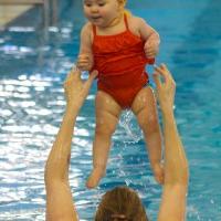 Woman throwing baby in red swim suit into the air