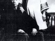 Chinese Couple - year unknown, both in elaborate  traditional chinese clothing, the man is seated and teh woman is standing