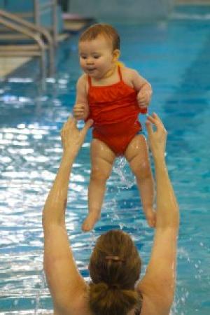 Woman throwing baby in red swim suit into the air